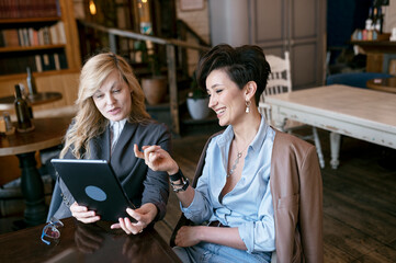 Two beautiful middle-aged women working on laptop and smiling.