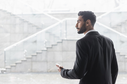 bi-racial security man with smartphone looking away in blurred hotel lobby.