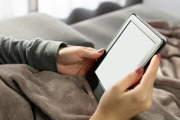 Hands of an unrecognizable young girl with painted nails holding an electronic book.