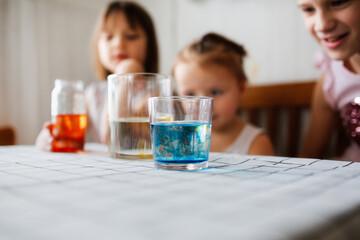 Three cute children play in the kitchen at home with colored liquids. Experiments with color at home.