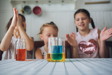 Three cute children play in the kitchen at home with colored liquids. Experiments with color at home.