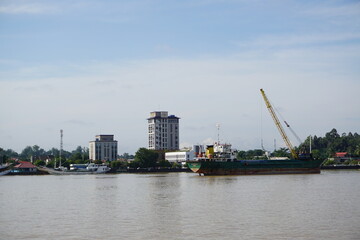 landscape photo of a loading ship with a crane on it on the Kalimantan river, and a city background, photo from far away