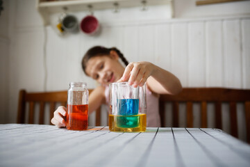 Caucasian kid girl play in the kitchen at home with colored liquids. Experiments with color at home.