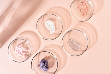Cosmetic products, scrub, face serum and gel in many petri dishes on a pastel beige background. Cosmetics laboratory research concept.