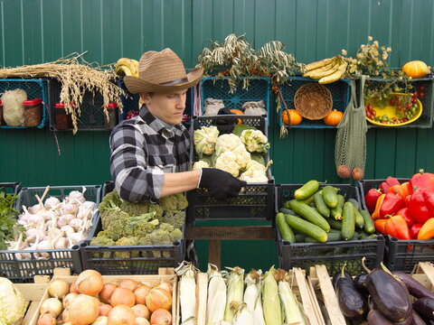 Cauliflower At The Farmers' Market. A Male Salesman Places A Box Of Cauliflower On The Counter. The Seller In A Protective Medical Mask.