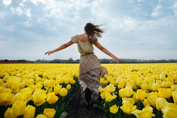 Dancing girl in a flower field full of yellow tulips in the Netherlands