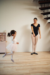 Fototapeta na wymiar Young mother and 3 years old daughter dancing classical ballet at home