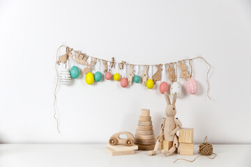 Fragment of the interior. Decorated children's room for Easter. A garland of plastic eggs and hares cut out of cardboard on the wall. Wooden rabbits and wooden cubes on the table.  Easter card.