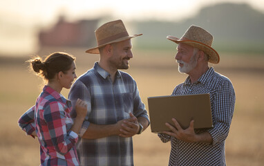 Three farmers with laptop talking in field during harvest