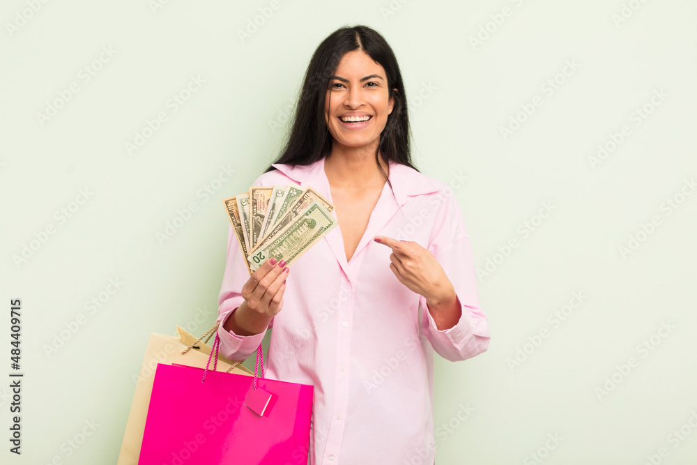 Wall mural young pretty hispanic woman smiling cheerfully, feeling happy and pointing to the side. shopping bags concept