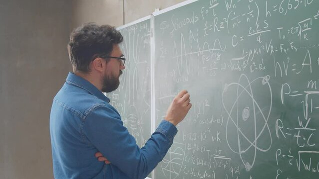 Teacher man writing math formulas on chalkboard with white chalk