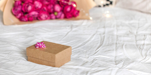 A gift box and a bouquet of roses are lying on the bed. Copy space.