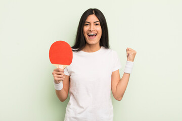 young pretty hispanic woman feeling shocked,laughing and celebrating success. ping pong concept