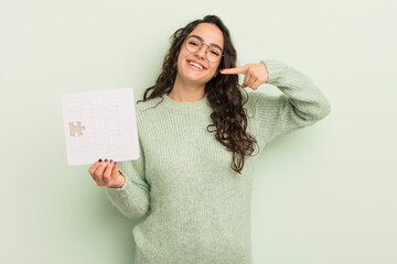 young pretty hispanic woman smiling confidently pointing to own broad smile. puzzle concept