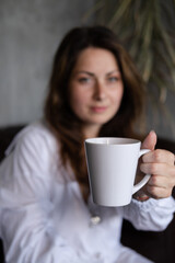 woman in white shirt on leather couch holding white cup. focus on mug. mock up. copy space.