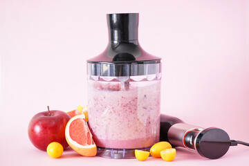 Black electric hand blender and accessories with fruits and smoothie on pink background