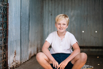 Cute blonde pre-teen boy with relaxed pose in rustic outdoor setting