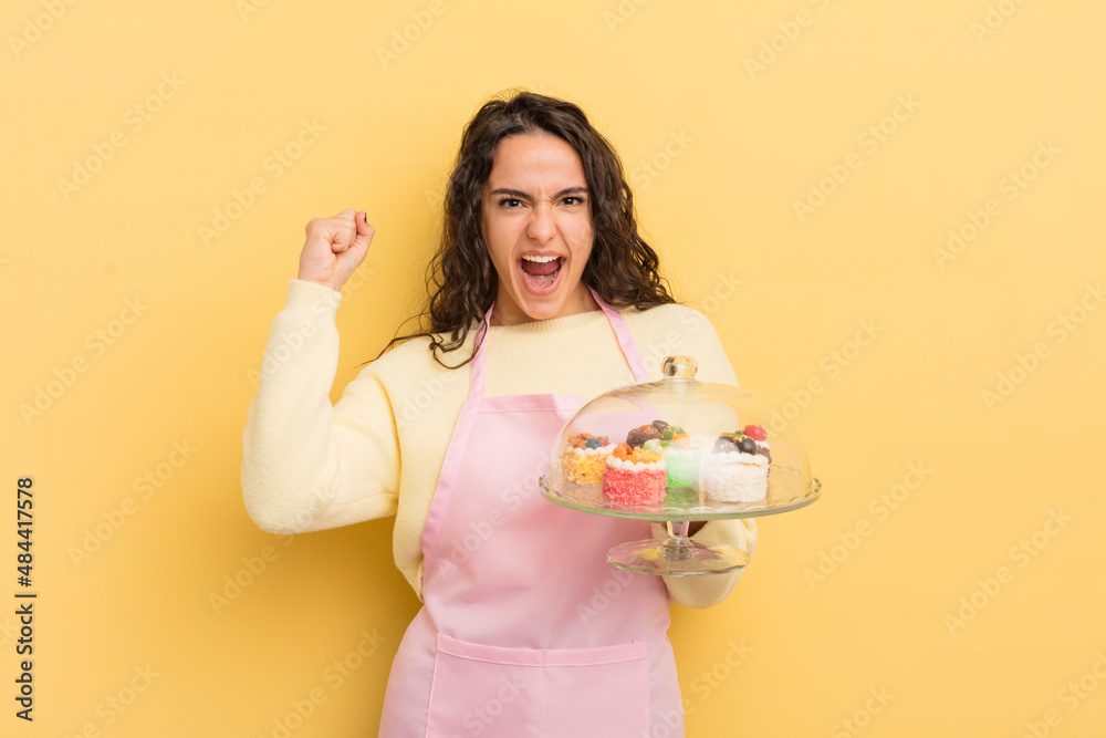 Wall mural young pretty hispanic woman shouting aggressively with an angry expression. chef and cakes concept