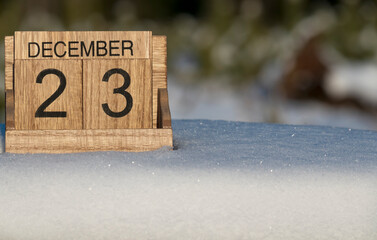 Wooden calendar of December 23 date standing in the snow in nature.
