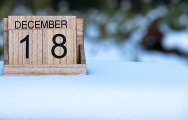Wooden calendar of December 18 date standing in the snow in nature.