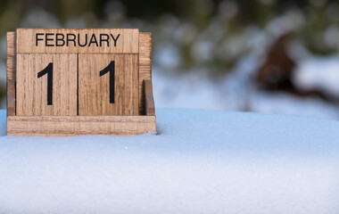 Wooden calendar of February 11 date standing in the snow in nature.