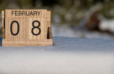 Wooden calendar of February 8 date standing in the snow in nature.