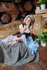 a cute little girl in a Cinderella costume sits on hay with bare legs near tulips for Easter....