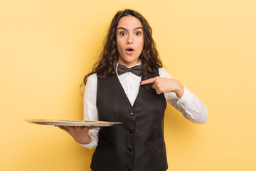 young pretty hispanic woman looking shocked and surprised with mouth wide open, pointing to self. waiter and tray concept - obrazy, fototapety, plakaty