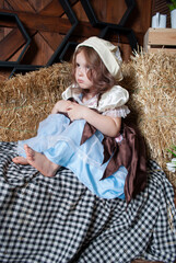 a cute little girl in a Cinderella costume sits on hay with bare legs near tulips for Easter....
