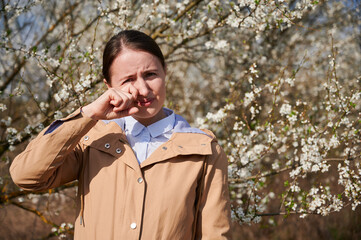 Woman allergic suffering from seasonal allergy at spring, posing in blossoming garden at...