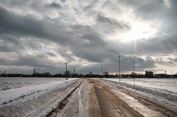 Winter muddy road between fields under clouds