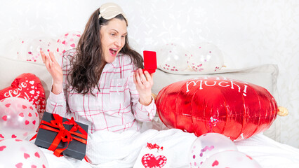 A beautiful woman in pink pajamas with a heart-shaped balloon lies on bed at home. Woman on Valentine's Day, birthday or anniversary. Love symbol
