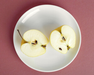 Apple halves on a white plate. Flat lay. Pink background 