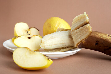 Shriveled yellow apples and overripe banana on a white plate. One apple is crushed into pieces. Selective focus. Light brown background