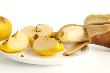 Yellow apples and overripe banana on a white background. One apple is cut into three pieces. The banana peel is ajar. Ugly food concept.