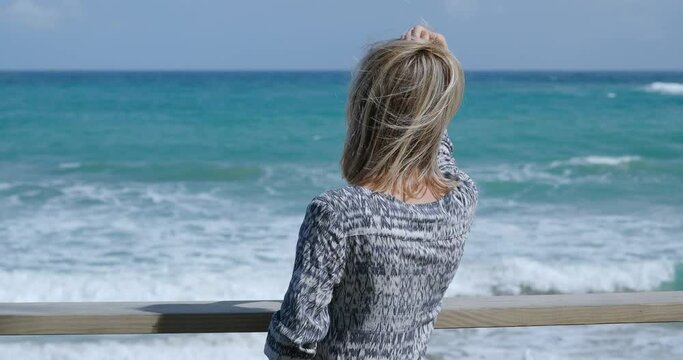 Happy caucasian woman wearing dress standing on terrace, enjoying at oceanside.