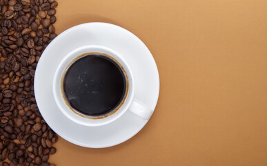 White cup of Americano black coffee without milk with a bunch of roasted coffee beans scattered from paper packaging. Coffee background, top view with copy space for logo or text.