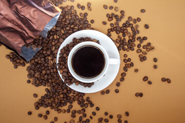 Naklejka premium White cup of Americano black coffee without milk with a bunch of roasted coffee beans scattered from paper packaging. Coffee background, top view with copy space for logo or text.