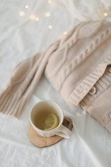 Obraz na płótnie Canvas Knitted beige sweater and cup of tea on messy bed background. Winter and spring fashion concept. Top view flat lay.