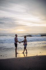 young beautiful couple in love walking at sunset by the ocean, couple relaxing in Bali, vacation in Bali, travel together, hug, love