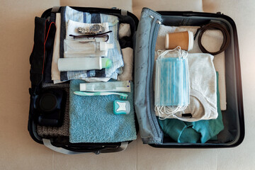 Happy  packing clothes into a suitcase, getting ready for a trip. Man packing passport, face masks and vaccination cartificate. Themes personal protection and flight rules during coronavirus pandemic.