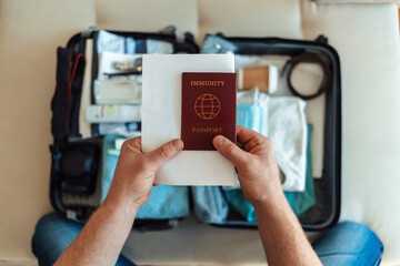 Preparing for travel in new normal. Man packing immunity passport, face masks and hand sanitizer. Themes personal protection and flight rules during coronavirus pandemic. People and travel concept.