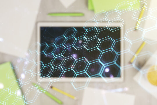Creative concept of wireless technology with hexagon hologram and modern digital tablet on background, top view. Big data and database concept. Multiexposure