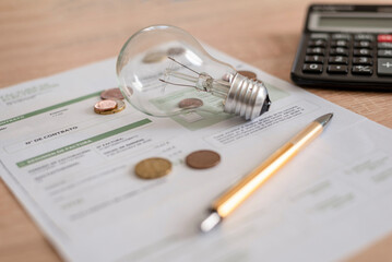 Electricity bill with light bulb, several coins, calculator and pen on the desk. Concept of...