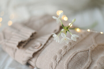 Fototapeta na wymiar Knitted beige sweater and delicate spring flower. Winter and spring fashion concept. 