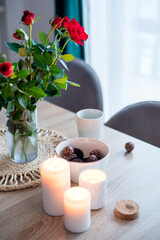 Coffee with sweets on the table, a vase with red roses and candles. Beautiful still life