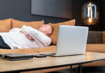 Exhausted mature businessman lying on sofa in office or at home and resting after hard work day. Overtime work or overload at work concept. High quality photo