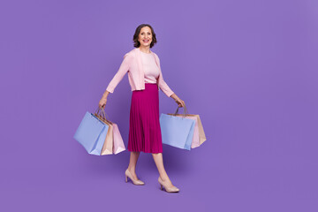 Full body profile portrait of positive pretty lady walk hold packages isolated on violet color background