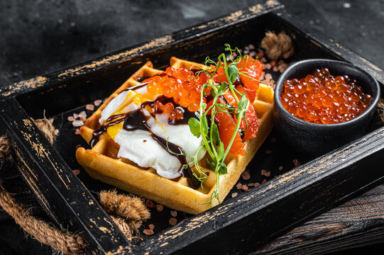 Delicious Waffle with smoked salmon fillet, poached egg and red caviar. Black background. Top view