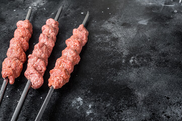 Raw mince lamb meat shish kebab on butcher table. Black background. Top view. Copy space